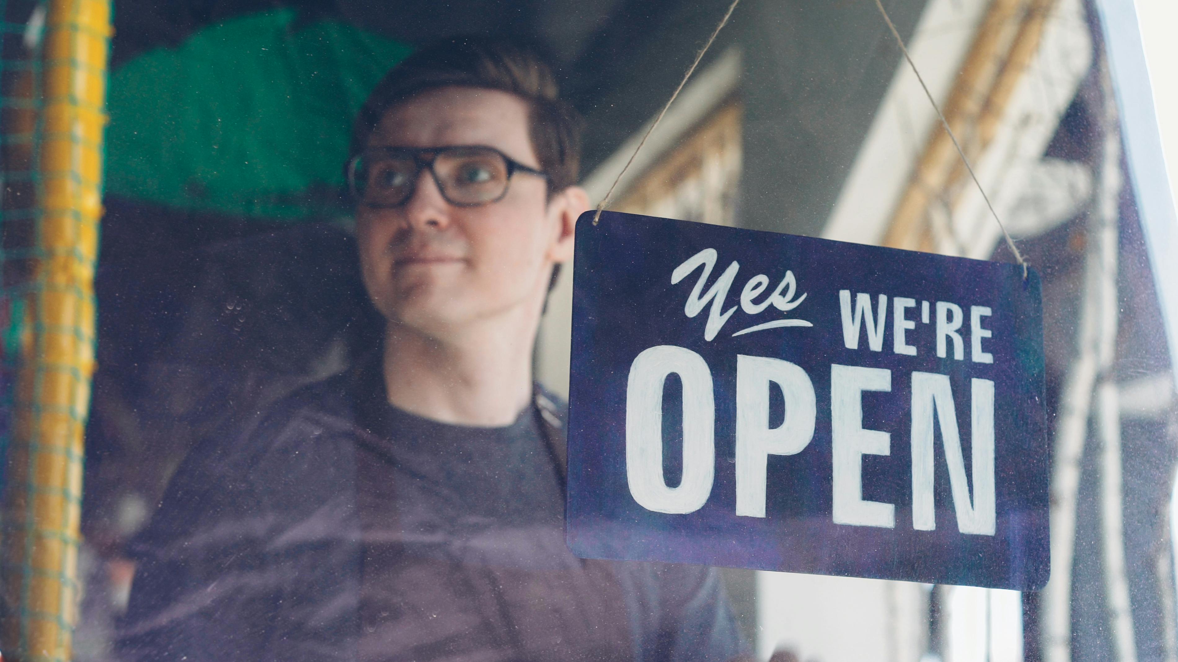 Small business owner standing behind an open sign in a storefront